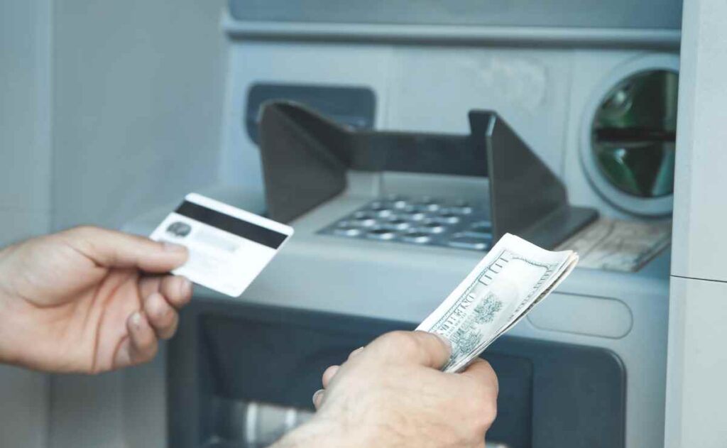 Person grabbing dollars and credit card at ATM because stimulus check payments will soon be sent in the State of Alaska