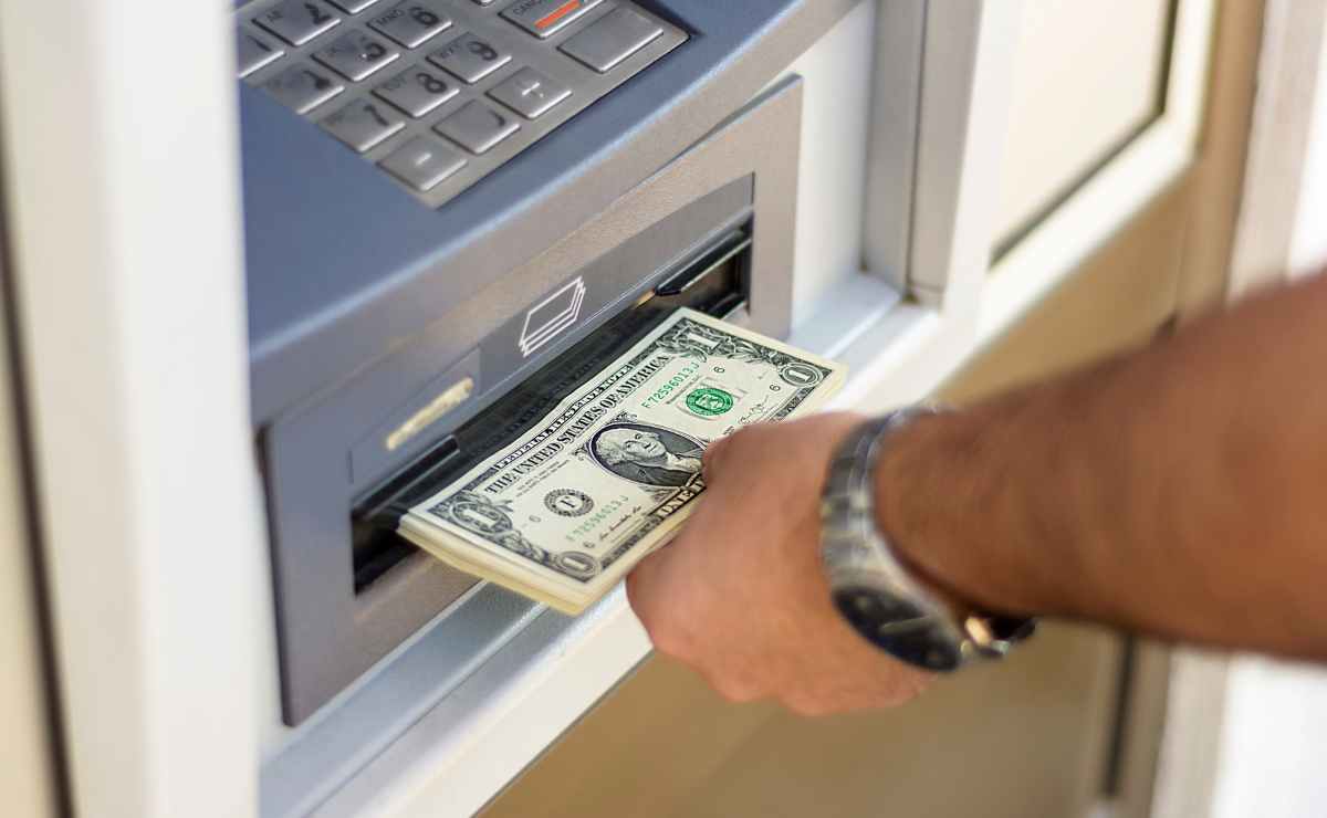 Man's hand taking dollars from ATM since these are the upcoming payments the Government will pay to Social Security beneficiaries