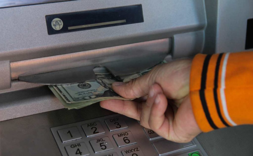 Hand with dollars at ATM for Social Security and SSDI amounts for 2024